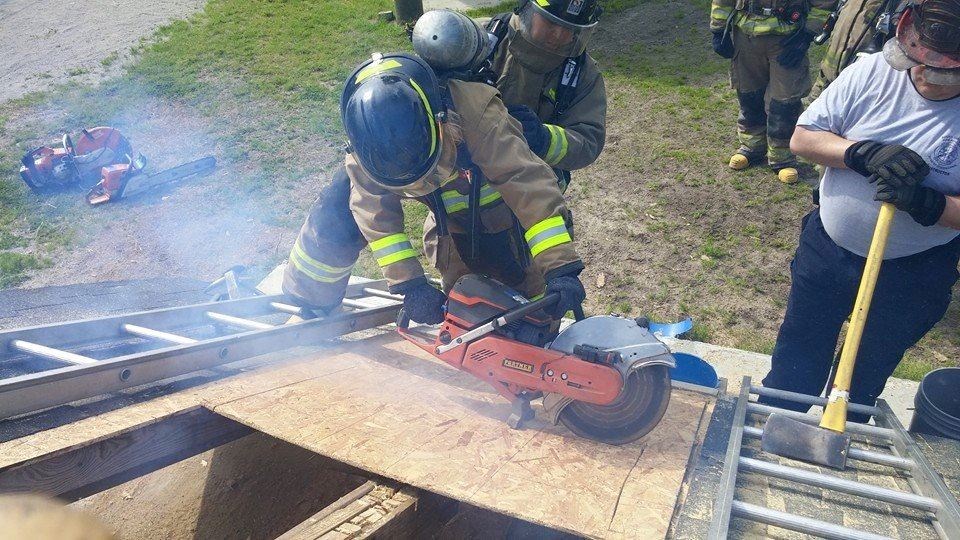 Firefighter Sawing Through a Plank While on a Ladder